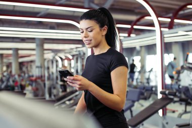 Genç Sporcu kadın koşu bandında koşarken akıllı telefon kullanıyor.