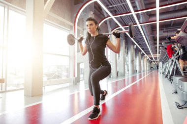 Modern spor salonunda kız halterle hamleler yapıyor.