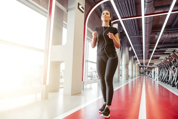 Frau mit Kopfhörern läuft auf Indoor-Bahn im Fitnessstudio — Stockfoto