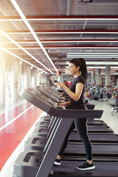 Sportswoman muda menggunakan smartphone saat joging di treadmill — Stok Foto