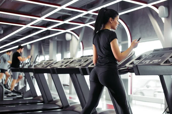 Sportswoman folosind smartphone-ul pentru antrenament app în timp ce jogging pe banda de alergare — Fotografie, imagine de stoc