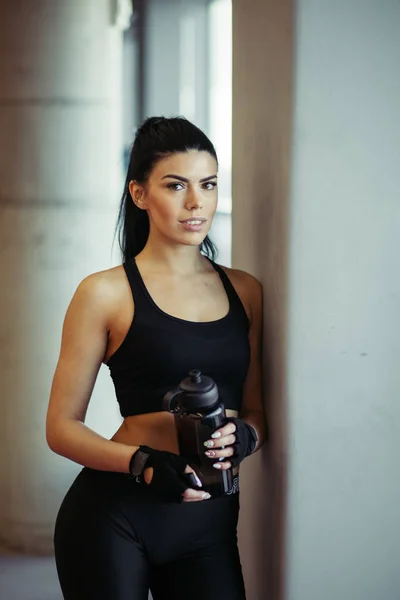 Modello femminile in posa con acqua dopo l'allenamento vicino alle finestre in palestra — Foto Stock