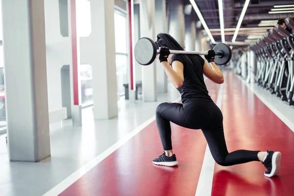 Meisje doet lunges met lange halter in moderne sportschool — Stockfoto