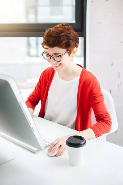 Kobieta pracuje w biurze, siedząc przy biurku, za pomocą komputera i patrząc na ekran — Zdjęcie stockowe