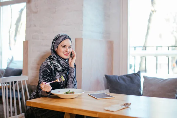 Joven mujer musulmana hablando por teléfono en la cafetería y mirando en la ventana — Foto de Stock