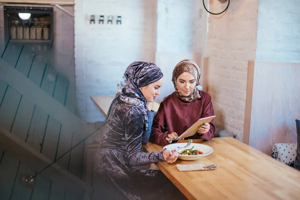 Dos mujeres musulmanas en la cafetería, comprar en línea usando tableta electrónica — Foto de Stock