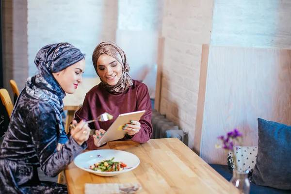 Dos mujeres musulmanas en la cafetería, comprar en línea usando tableta electrónica — Foto de Stock