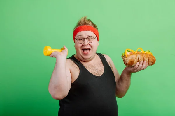 Alegre grasa macho haqving diversión con hamburguesa y dumbbell —  Fotos de Stock