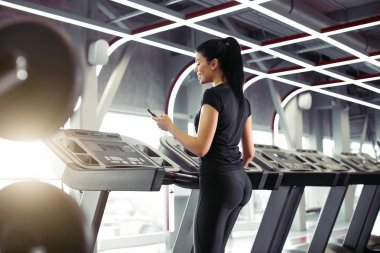 Sporcu kadın koşu bandında koşarken egzersiz uygulaması için akıllı telefon kullanıyor