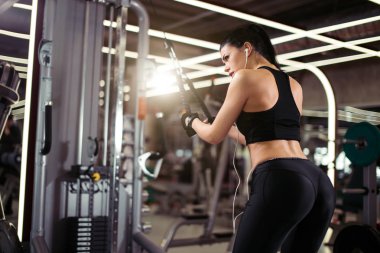 Dikiz görüşlü, formda bir kadın spor salonunda egzersiz makinası kablolu yayını ile egzersiz yapıyor.