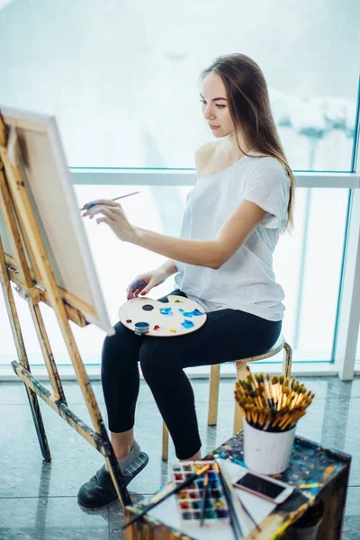 Donna artista che dipinge un quadro in uno studio ben illuminato — Foto Stock