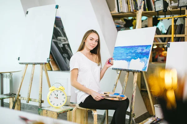Mulher artista pintando um quadro no cavalete com tintas a óleo em sua oficina — Fotografia de Stock