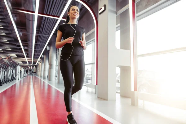 Frau mit Kopfhörern läuft auf Indoor-Bahn im Fitnessstudio — Stockfoto