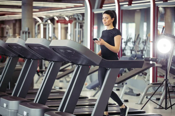 Ung Sportswoman använder smartphone medan jogging på löpband — Stockfoto