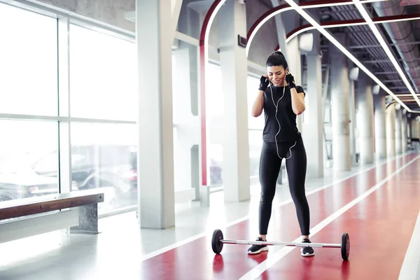Fitte junge Frau steht im Fitnessstudio und hört Musik mit Hanteln auf dem Boden — Stockfoto