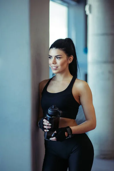 Modèle d'ajustement féminin posant avec de l'eau après l'entraînement près des fenêtres dans la salle de gym — Photo