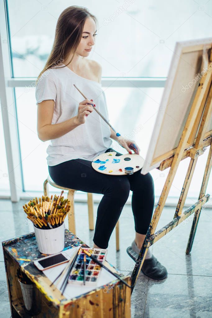 Painter, european girl drawing sea-scape on canvas in her workshop. Concept of fine-art classes