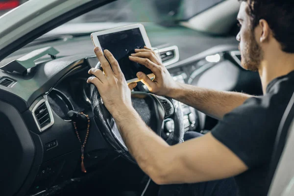 Mechaniker sitzt im Auto und schaut in der Garage auf digitales Tablet — Stockfoto