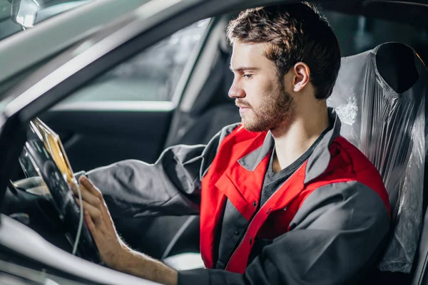 Mechanik siedzi w samochód patrząc na cyfrowy Tablet w garażu — Zdjęcie stockowe