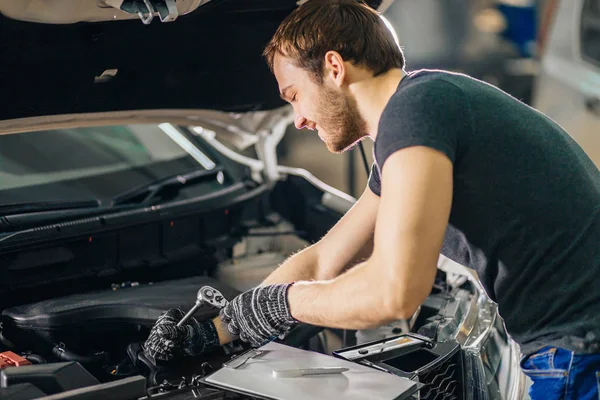 Mecánico que trabaja bajo el capó del coche en el garaje de reparación — Foto de Stock