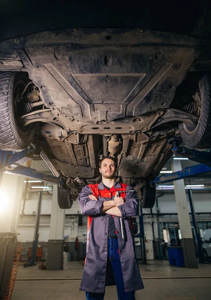 Meccanico sotto sollevato auto loking fotocamera e mani incrociate — Foto Stock