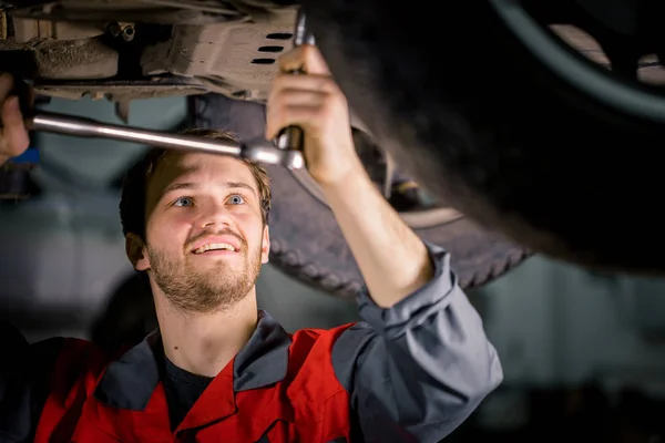 Mecánico debajo del coche en garaje examinando neumático y condición técnica — Foto de Stock
