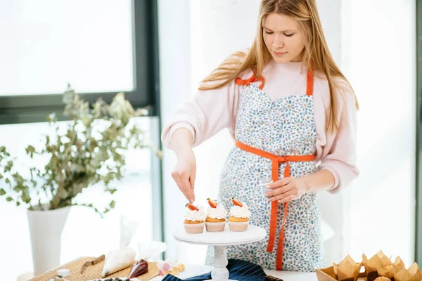 Jolie jeune femme décorant des cupcakes sur sa cuisine — Photo