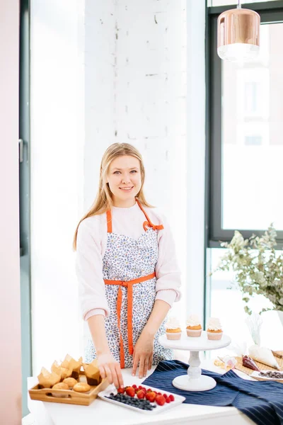 Feliz rubia pastelera hembra en proceso de preparación de cupcakes —  Fotos de Stock