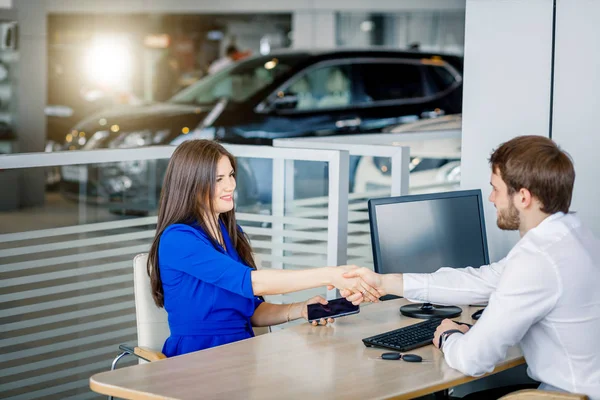 Gerente de ventas y cliente femenino dándose la mano felicitándose mutuamente en la sala de exposición del concesionario . — Foto de Stock