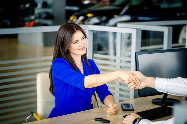 Responsabile commerciale e cliente femminile che si stringono la mano congratulandosi a vicenda nello showroom della concessionaria . — Foto Stock