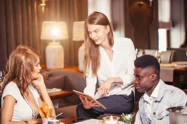 Gruppo di studenti che discutono le foto sul tablet digitale nel caffè — Foto Stock