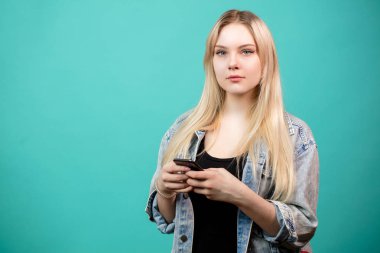 Neşeli genç beyaz kadın mavi üzerine akıllı telefon kullanıyor.