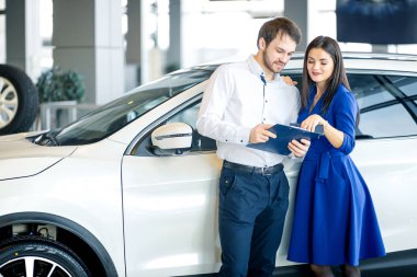 Happy couple choosing a car in dealership clipart