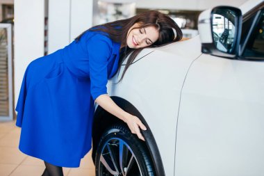 Araba galerisini ziyaret ediyorum. Genç bir kadın yeni arabasına sarılıyor.
