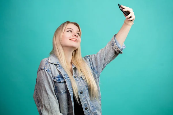 Mujer rubia positiva tomando selfie sobre fondo azul aislado burlándose de sí misma — Foto de Stock