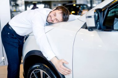 Yakışıklı adam galeride yeni arabasını kucaklıyor.