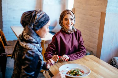 Two Muslim women in cafe, friends meeting clipart