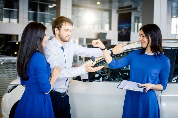 Car salesgirl giving the key of the new car to the attractive couple owners. — Stock Photo, Image