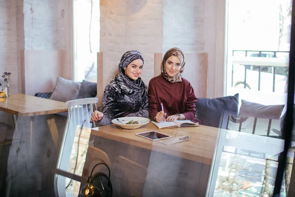 Две симпатичные мусульманки в головном шарфе пишут в блокноте — стоковое фото