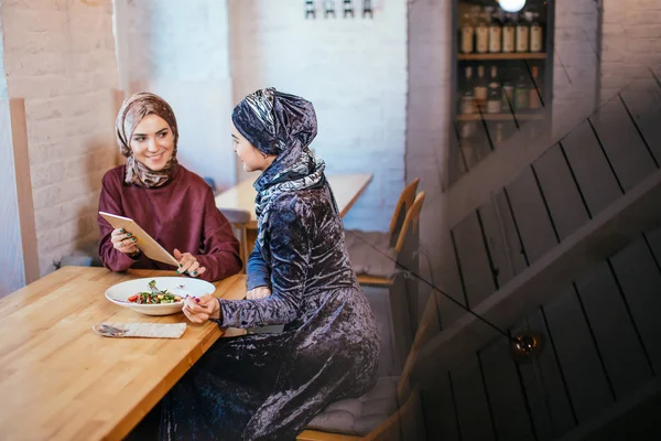 Две мусульманки в кафе, делают покупки онлайн с помощью электронного планшета — стоковое фото