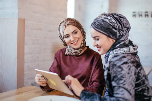 Dos mujeres musulmanas en la cafetería, comprar en línea usando tableta electrónica — Foto de Stock