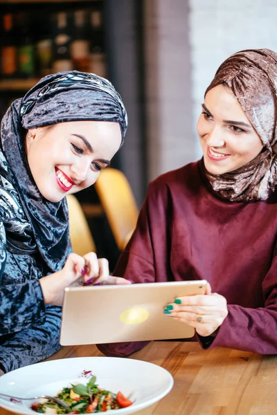 Dos mujeres musulmanas en la cafetería, comprar en línea usando tableta electrónica — Foto de Stock