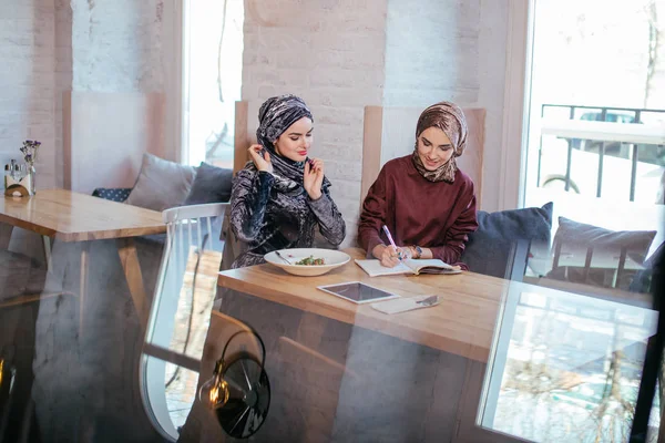 Duas mulheres de negócios muçulmanas bonitas no cachecol cabeça escrever no caderno — Fotografia de Stock
