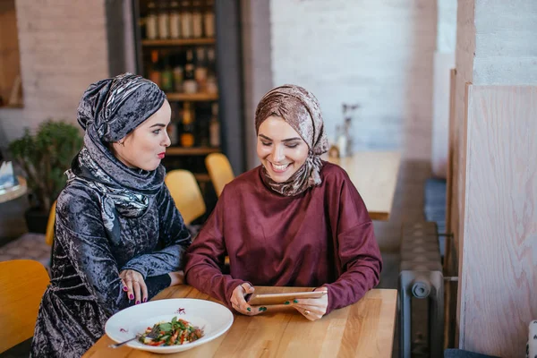 Dos mujeres musulmanas en la cafetería, comprar en línea usando tableta electrónica — Foto de Stock