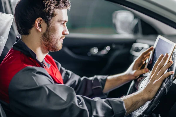 Mechaniker sitzt im Auto und schaut in der Garage auf digitales Tablet — Stockfoto