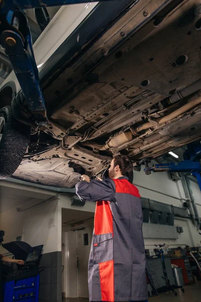 Meccanico sotto auto in garage esame pneumatici e condizioni tecniche — Foto Stock