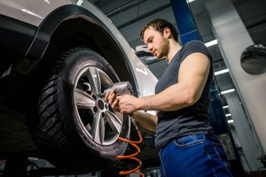 mechanic changing car wheel in auto repair garage clipart