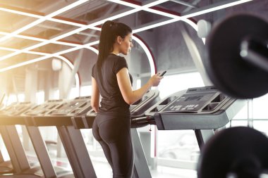 Sporcu kadın koşu bandında koşarken egzersiz uygulaması için akıllı telefon kullanıyor