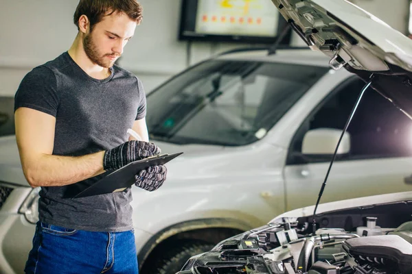 Mechachic controleren op auto motor en maken van aantekeningen in Klembord — Stockfoto