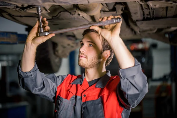 Mecânico sob carro na garagem examinando pneu e condição técnica — Fotografia de Stock